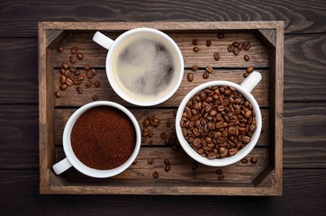 Different types of coffee - ground, grain and beverage on dark wooden background, top view, horizontal.