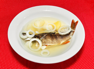Fish soup in a white plate on a red background