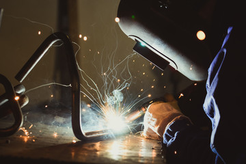 Industrial workshop man welding round pipe on a work table, producing blue smoke, yellow sparks and...
