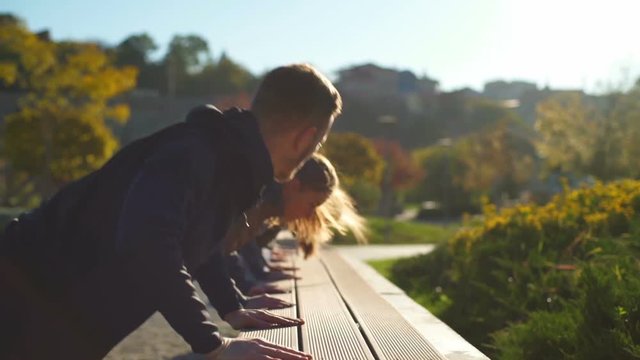 A group of young friends doing push ups in the beautiful park slow motion