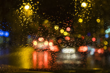 Blurred car lights on circle spotlights on a wet water drops glass dark abstract scene