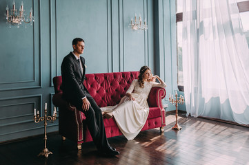 Obraz premium cute wedding couple in the interior of a classic studio posing at the sofa . hey kiss and hug each other, holding hands looking at each other