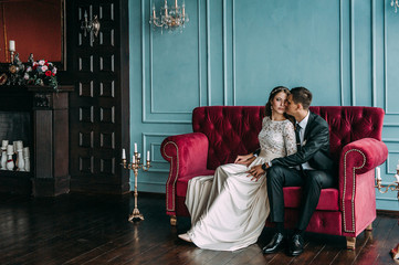 Obraz na płótnie Canvas cute wedding couple in the interior of a classic studio posing at the sofa . hey kiss and hug each other, holding hands looking at each other