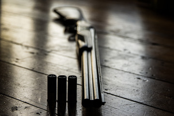 Shotgun charged with bullets and spare bullets on wooden floor,