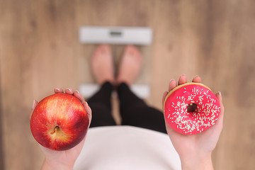 Close up view of woman making choice between apple and donut with blurred scales on background....