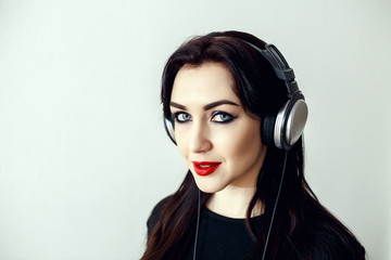 Happy pretty smiling woman with red lips in a black jacket listens to music in headphones over white background