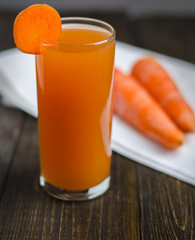 glass of carrot juice and fresh carrots on wooden table