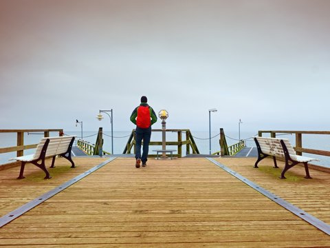 Tourist with red backpack on wooden sea pier. Man in trekking suit