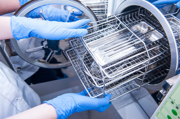 Dentist assistant's hands get out sterilizing medical instruments from autoclave. Selective focus
