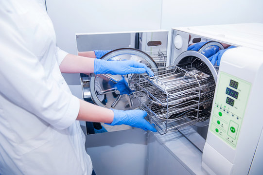 Dentist assistant's hands get out sterilizing medical instruments from autoclave. Selective focus