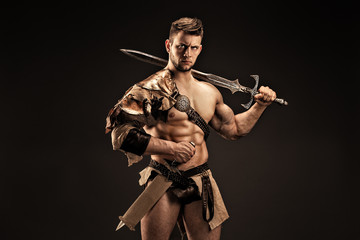 Portrait of angry gladiator with sword looking up against of black background. Isolated