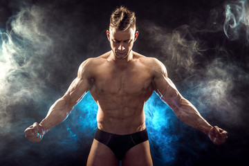 Handsome power athletic man bodybuilder. Fitness muscular body on dark smoke background. Perfect...