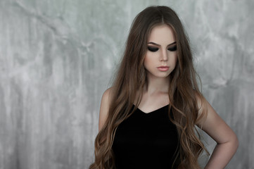 Fototapeta premium Young girl with long beautiful hair and smoky eyes wearing black maxi evening dress. Studio shot