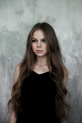 Fototapeta premium Young girl with long beautiful hair and smoky eyes wearing black maxi evening dress. Studio shot