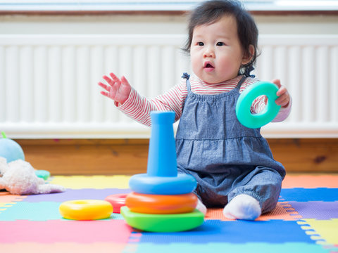 Adorable baby girl sitting on play mat and playing toy at home