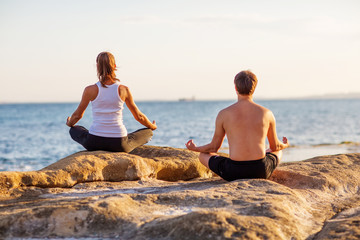 Fototapeta premium Young couple practicing yoga on the beach at sunset