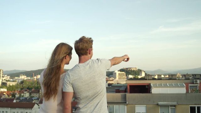 CLOSE UP: Lovers standing on rooftop looking on stunning city pointing fingers