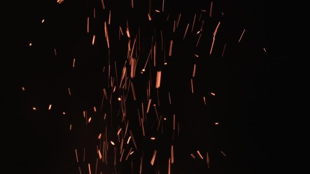 Large amount of sparks rise from the flames from fire against black background.