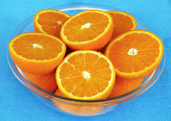 Halves of oranges in glass bowl on blue table clothe