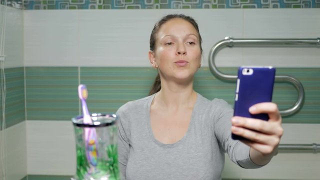 Young attractive woman doing selfie phone in the bathroom of the hotel room. She smiles and changes the posture for a better photo