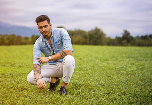 Handsome young man at countryside, in front of field or grassland, wearing shirt, looking at camera
