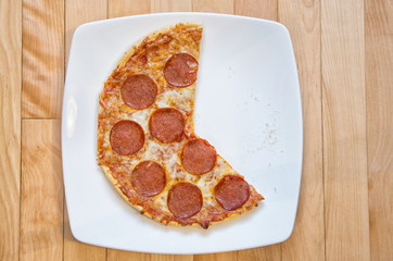 Consumed pepperoni and cheese pizza in white plate over a wooden background