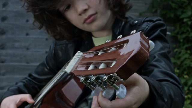 4k Shot of a Cute Child Outside Tuning his Guitar