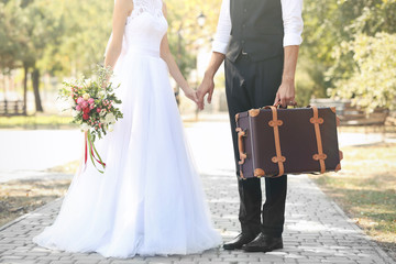 Groom and bride with vintage suitcase walking in park