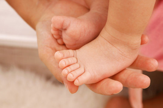 Woman hand holding bare baby feet, close up view