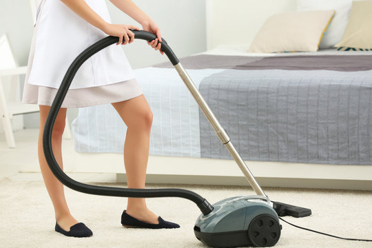 Chambermaid cleaning room with vacuum cleaner