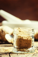 Ground ginger in a glass jar and fresh ginger root, vintage wood