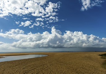 Fototapeta na wymiar View across deserted beach low tide beautiful clouded sky mid winter.