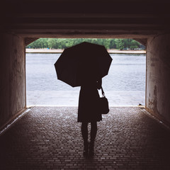 Girl with umbrella standing in the underpass. Against the background of the tunnel with a bright sun illuminates the landscape of nature. Vertical image. Overall plan.