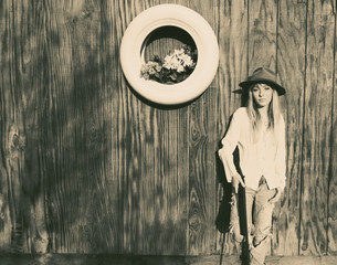 Woman with gun leaning against a wooden wall with white tire with flowers.