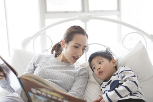 Mother is showing her picture book to her son in bed