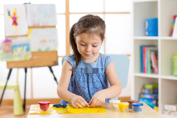 Kid girl plays plasticine or dough at home in her room