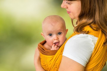 Happy mother with her baby in a sling - isolated on green