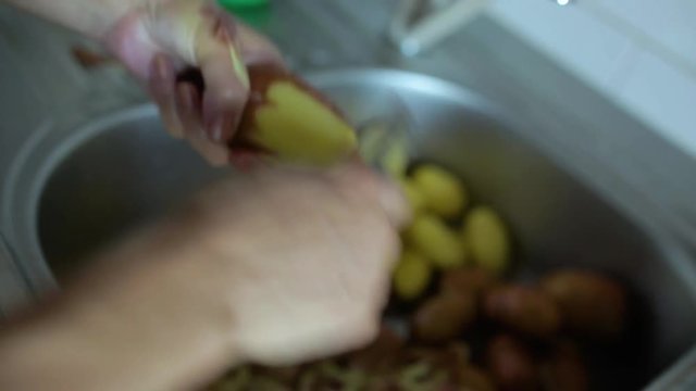 Closeup of woman's hands peeling potatoes in the sink