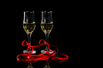 two glasses with champagne and red ribbon on black background