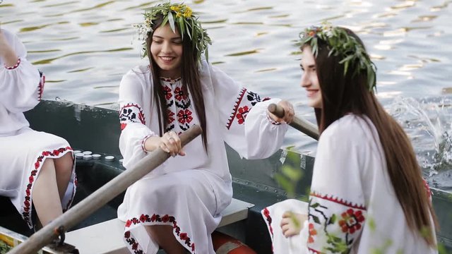Three girls in the Slavic national dress floating in a boat on the river. Girls in wreaths fun laugh. national traditions. girls in embroidered shirts.