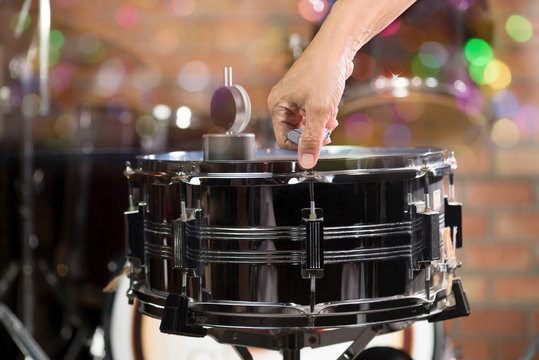  Hand adjusting tension rod of snare drum.Drummer measuring batter tension with drum dial and tuning tension rod for a proper sound.Copy space ,multicolour bokeh background.