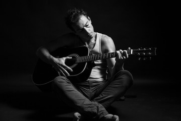 Black and white, low key portrait of caucasian man that play his acoustic guitar