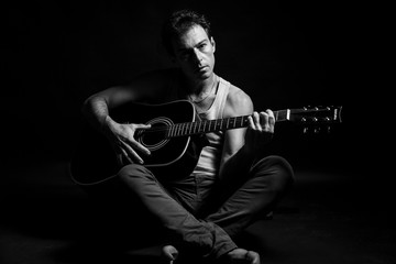 Black and white, low key portrait of caucasian man that play his acoustic guitar
