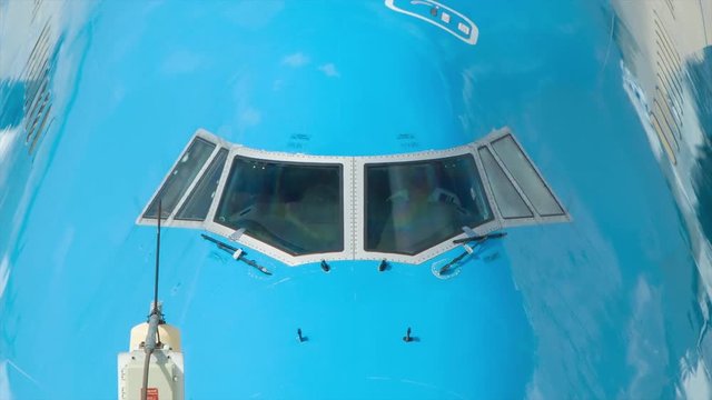 Blue Unmarked Boeing 747 Commercial Passenger Jet Airliner Cockpit Close-up from Outside with Two Pilots seen Inside during a Sunny Day