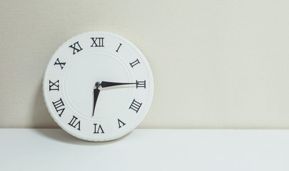 Closeup white clock for decorate show a quarter past six or 6:15 a.m. on white wood desk and cream wallpaper textured background with copy space
