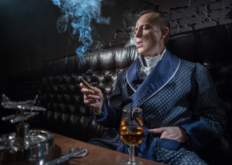 Man in his office smoking a cigar and drinking brandy