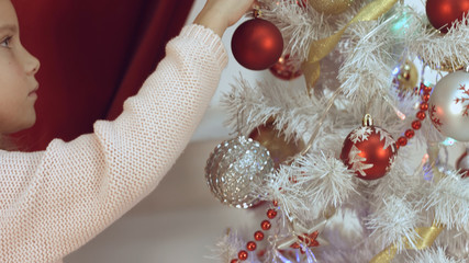 Naklejka premium Girl hangs Christmas balls at christmas tree