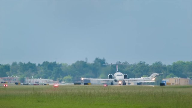 Business Jets Taking Off from Airport Viewed from Front with Runway Lights and Green Grass at Dusk