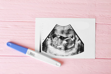 Ultrasound photo and pregnancy test on pink wooden background