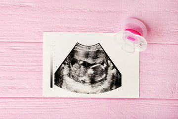 Ultrasound photo and pacifier on pink wooden background